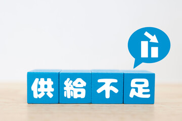 Fototapeta premium 供給不足をイメージする下降グラフ。青いブロック文字で「供給不足」と表示。コピースペースあり