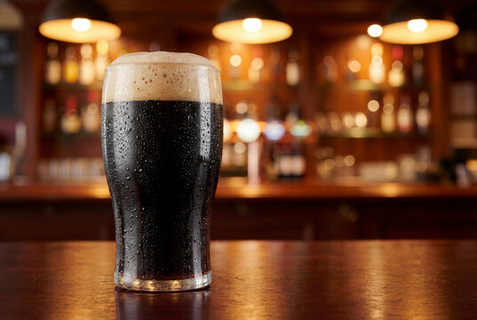 Glass of dark stout beer with foam head on bar counter