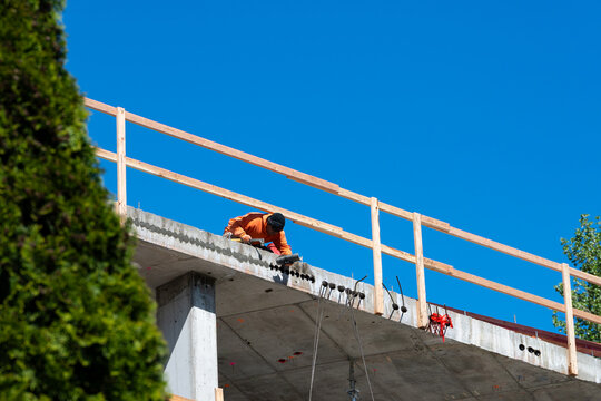 Construction worker high up on building project working on grouting structural post-tensioning wire strand holes running through concrete slab of floor
