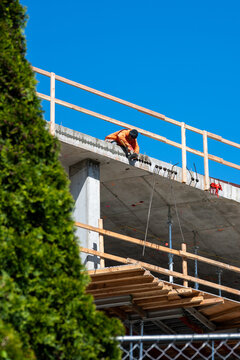 Construction worker high up on building project working on grouting structural post-tensioning wire strand holes running through concrete slab of floor
