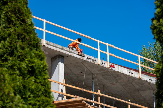 Construction worker high up on building project working on grouting structural post-tensioning wire strand holes running through concrete slab of floor
