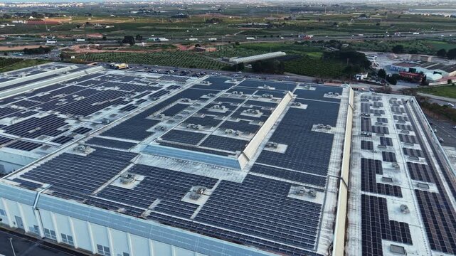 A large building has many solar panels installed on its roof. The views show green fields and distant rural landscapes under a clear sky. Sunlight highlights the panels during daytime.