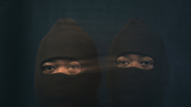 Two ghostly views of a male in a brown balaclava appear horizontally merged through an intense side by side motion blur stretching across their eyes. The unsettling visual distortion