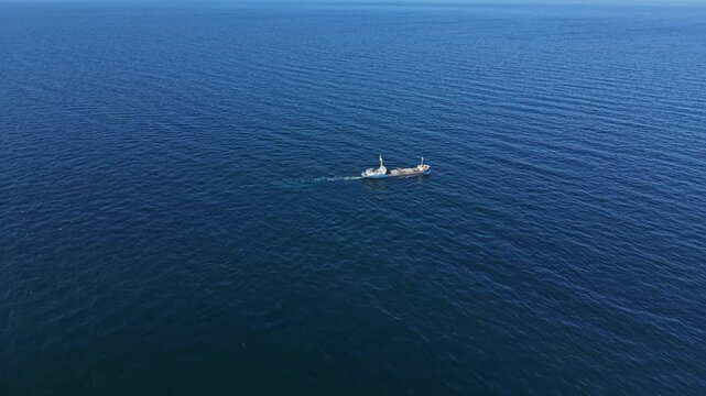 A fishing boat moves steadily across the deep blue water of the ocean. The crew works together while the sun shines above them. The vastness of the sea surrounds them.