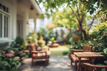 Fototapeta premium A softly blurred view showcases a tranquil outdoor patio area with wooden furniture nestled amongst lush greenery and a charming house facade.