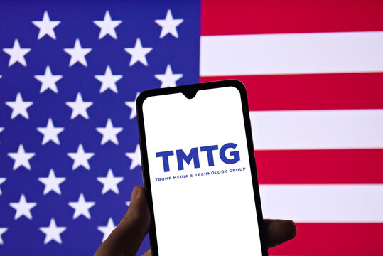 TMTG (Trump Media and Technology Group) logo on a smartphone screen with the United States flag in the background.