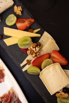 cheeseboard with fruit, cava, and iberian ham charcuterie on black table, contrast