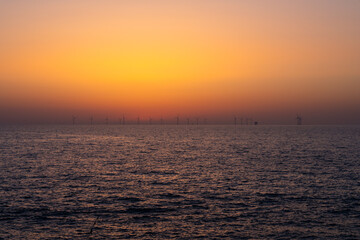 Obraz premium Offshore Wind Farm Silhouettes Against Golden Twilight Sky