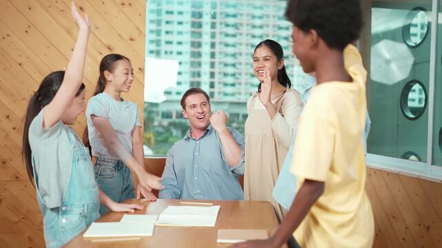 Caucasian teacher and diverse children putting hand together to celebrate successful project or encourage in classroom. Represent love, corporate, team working, togetherness and unity. Edification