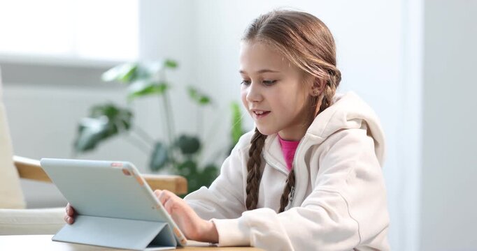 Little girl using modern tablet at wooden table indoors