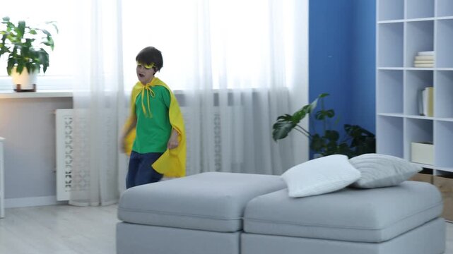 Little boy in superhero costume running around pouffe at home. Camera moving