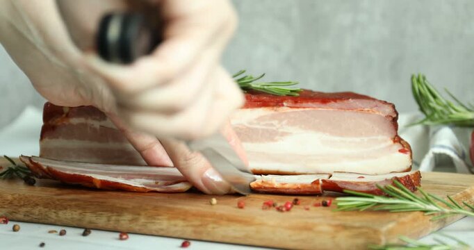 Woman cutting smoked bacon at light table against grey background, closeup