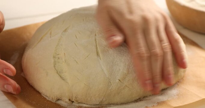 Woman putting flour onto loaf of raw sourdough bread on white table, closeup