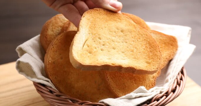 Woman taking browned toast bread slice from wicker basket at table, closeup