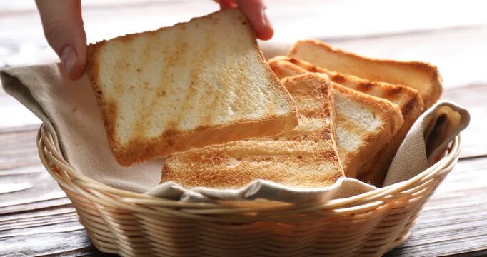 Woman taking browned toast bread slice from wicker basket at wooden table, closeup