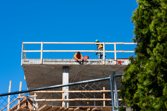 Construction worker high up on building project working on grouting structural post-tensioning wire strand holes running through concrete slab of floor
