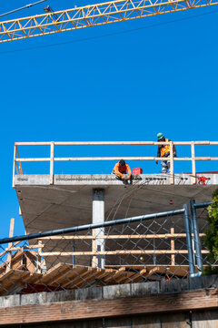 Construction worker high up on building project working on grouting structural post-tensioning wire strand holes running through concrete slab of floor
