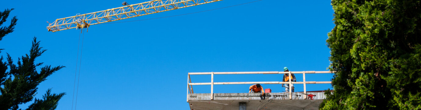 Construction worker high up on building project working on grouting structural post-tensioning wire strand holes running through concrete slab of floor
