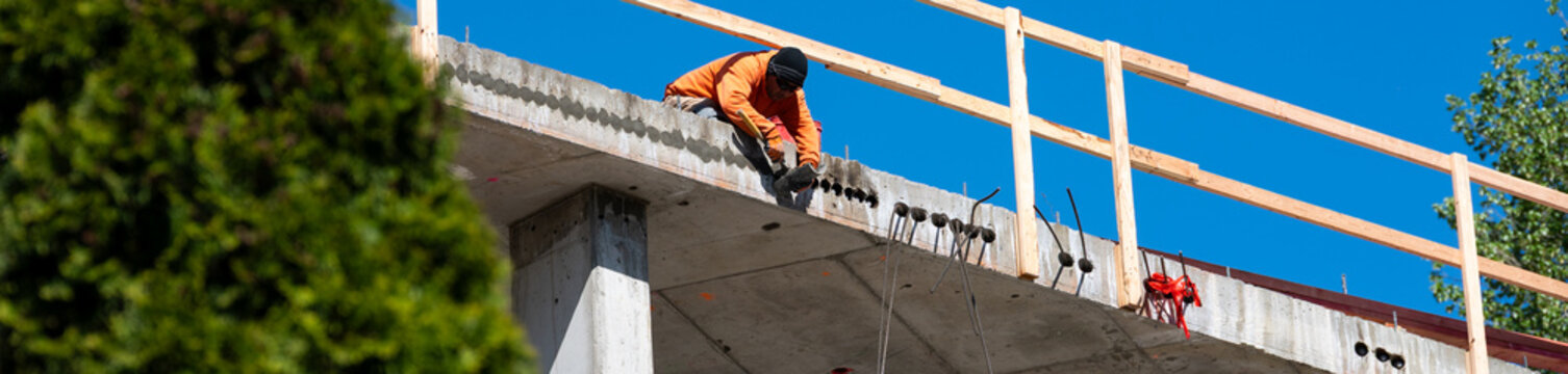 Construction worker high up on building project working on grouting structural post-tensioning wire strand holes running through concrete slab of floor
