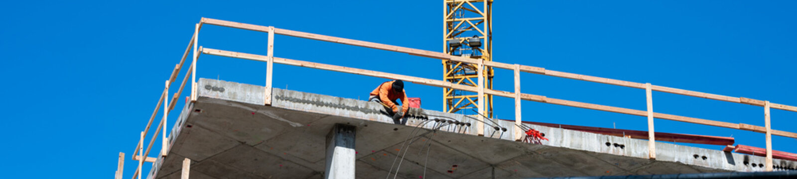 Construction worker high up on building project working on grouting structural post-tensioning wire strand holes running through concrete slab of floor
