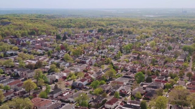 A wide-angle drone shot gently panning left over a dense residential area with lush green trees and diverse family homes during a bright spring day, ideal for real estate and suburban lifestyle