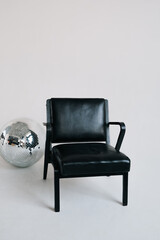 A black chair stands in a white studio beside a silver disco ball, creating a simple modern interior scene.