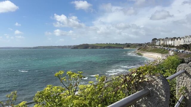 Stunning wide angle footage captures Gyllyngvase Beach and Pendennis Point in Falmouth, Cornwall, UK under clear daylight with dynamic waves, vibrant greenery, coastal town, and dramatic sky. (200)