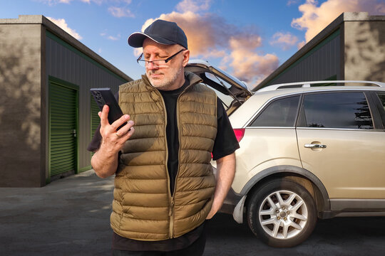 Man uses smartphone near car and storage units, arranging self storage access or moving service.