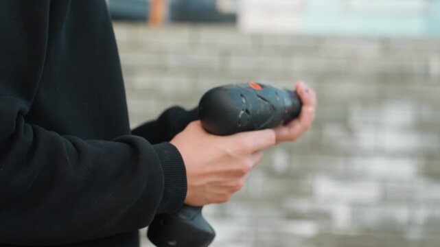 Closeup hands adjusting drill bit, careful inspection against urban concrete backdrop, steady palm and finger movements tuning torque and position, instructional mood with technical focus