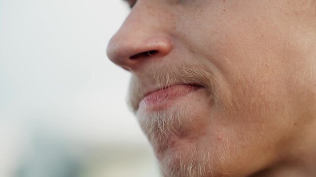 Closeup young man thinker pressing lips together in quiet contemplation, soft overcast light highlights textured skin and faint mustache, subtle microexpression conveying introspective mood
