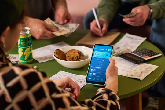 Young adults managing shared expenses, counting cash, checking bills, sending mobile payment on smartphone. Useful for budgeting, student finance, roommate cost sharing marketing