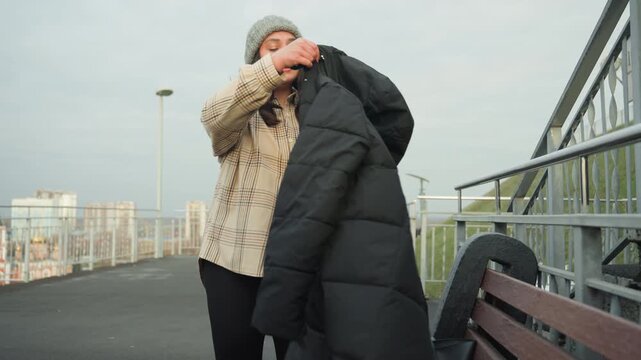 Confident dance act. Animated woman dons puffer jacket. Vibrant woman in coat moves confidently on city rooftop. Dynamic black woman prepares for departure with lively rooftop dance and fashion style
