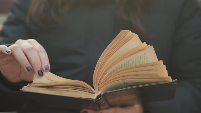 Reading in city. Student flipping through pages attentively. Focused student reads pages outdoors in city environment. Student concentrates on reading pages on bench amidst soft city background