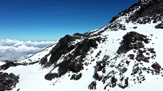 Aerial view, moving over an in snow covered mountain summit with clouds in the background