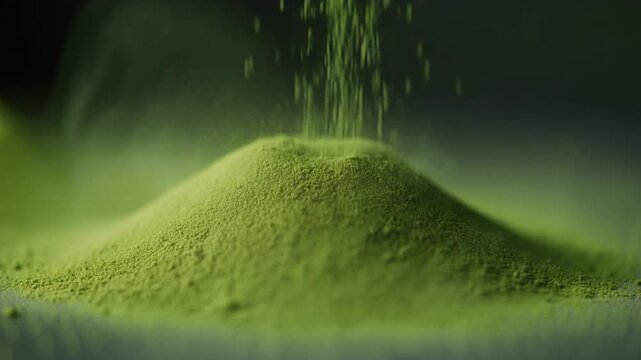 Green matcha powder cascades onto a heap creating a dust cloud. Great for promoting wellness, tea products, kitchen supplies, and organic goods.