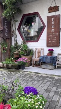 Charming traditional Chinese tea house entrance in Suzhou, featuring hexagonal window, blooming chrysanthemums, bamboo, and antique wooden furniture in spring.