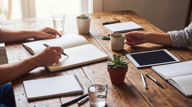 Two people collaborating at a rustic wooden table, writing notes and discussing ideas in a comfortable setting.