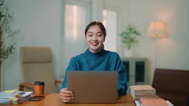 Happy young asian woman opening her laptop to start a new day of work. Cheerful female professional starting her workday with a smile