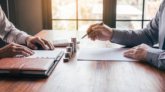 Business partners discussing financial strategies with stacks of coins and documents on a wooden table.