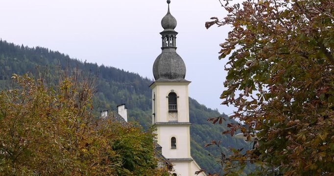 White alpine church bell tower standing against mountain forest