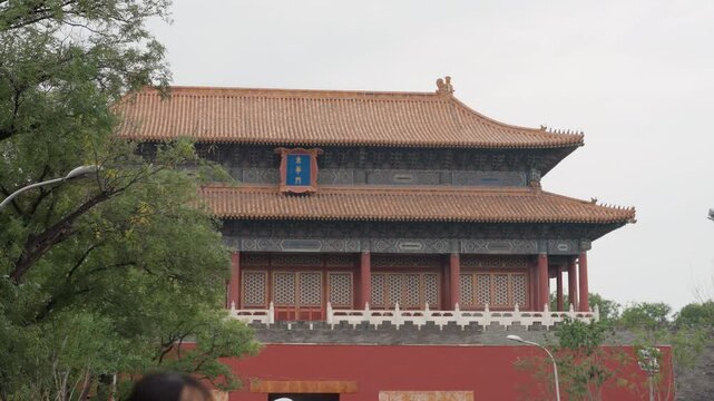 Wide view imperial gate framed trees with tiled roof and decorated facade, tour guide leading group across courtyard, lush greenery under overcast sky, travel vibe and cultural landmark activity