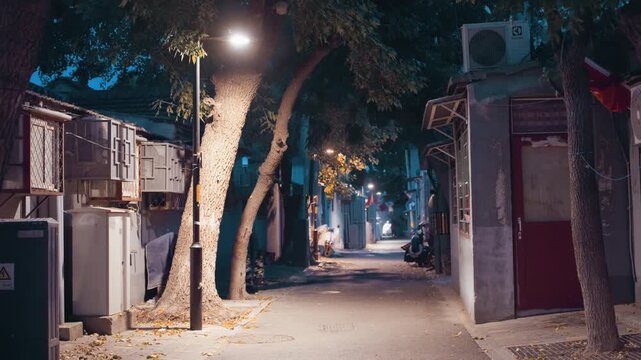Night alley empty under warm lamp, leafstrewn pavement flanked by old shopfronts and bowed trees, soft amber glow mixing with cool teal background, cinematic stillness and nostalgic atmosphere, slow