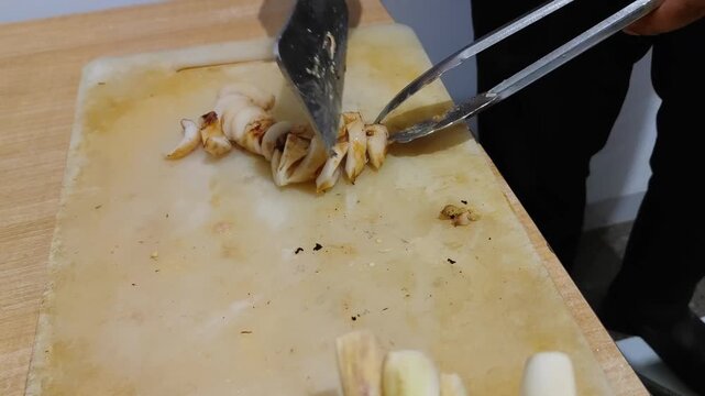 Close-up video of freshly grilled squid being sliced on a cutting board using kitchen tongs and scissors. Delicious seafood preparation process, perfect for culinary, street food, and cooking concept 