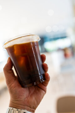 Close up of take away plastic cup of iced black coffee in hand
