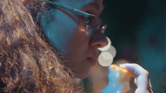 Nighttime street close up woman with glasses, curly hair, bokeh lights, neon glow latenight snack moment, contemplative gaze, slow breath, subtle film grain, candid festival or cinema queue vibe,