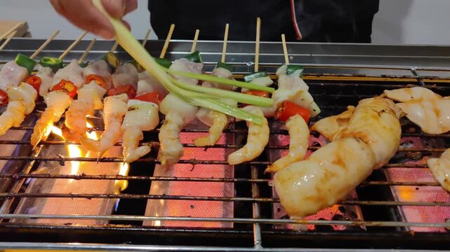 Close-up video of shrimp skewers being grilled over charcoal fire with vegetables such as chili and green onions. Delicious seafood street food, smoky barbecue atmosphere, perfect for culinary