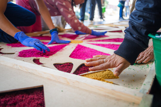 Close-up of artisan hands placing colored sawdust to create a monumental rug during Holy Week in Cholula, Puebla, Mexico.