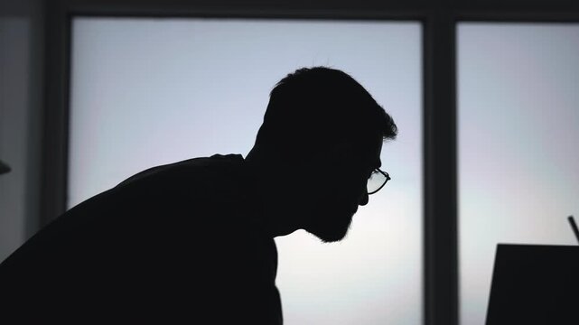 Contemplative Man By Window. Leaning Figure Of Man Lost In Thought At His Laptop Near Lit Window. Media