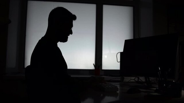 Contemplative Man By Window. Leaning Figure Of Man Lost In Thought At His Laptop Near Lit Window. Media