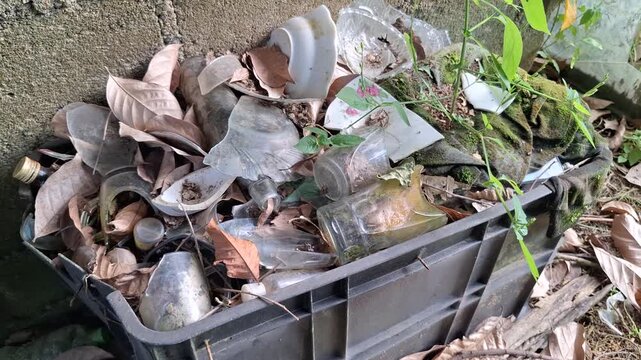 Pile of Broken Glass Bottles and Ceramic Plates Waste Inside Plastic Container in Backyard, Concept of Inorganic Household Trash and Environmental Pollution during Daylight